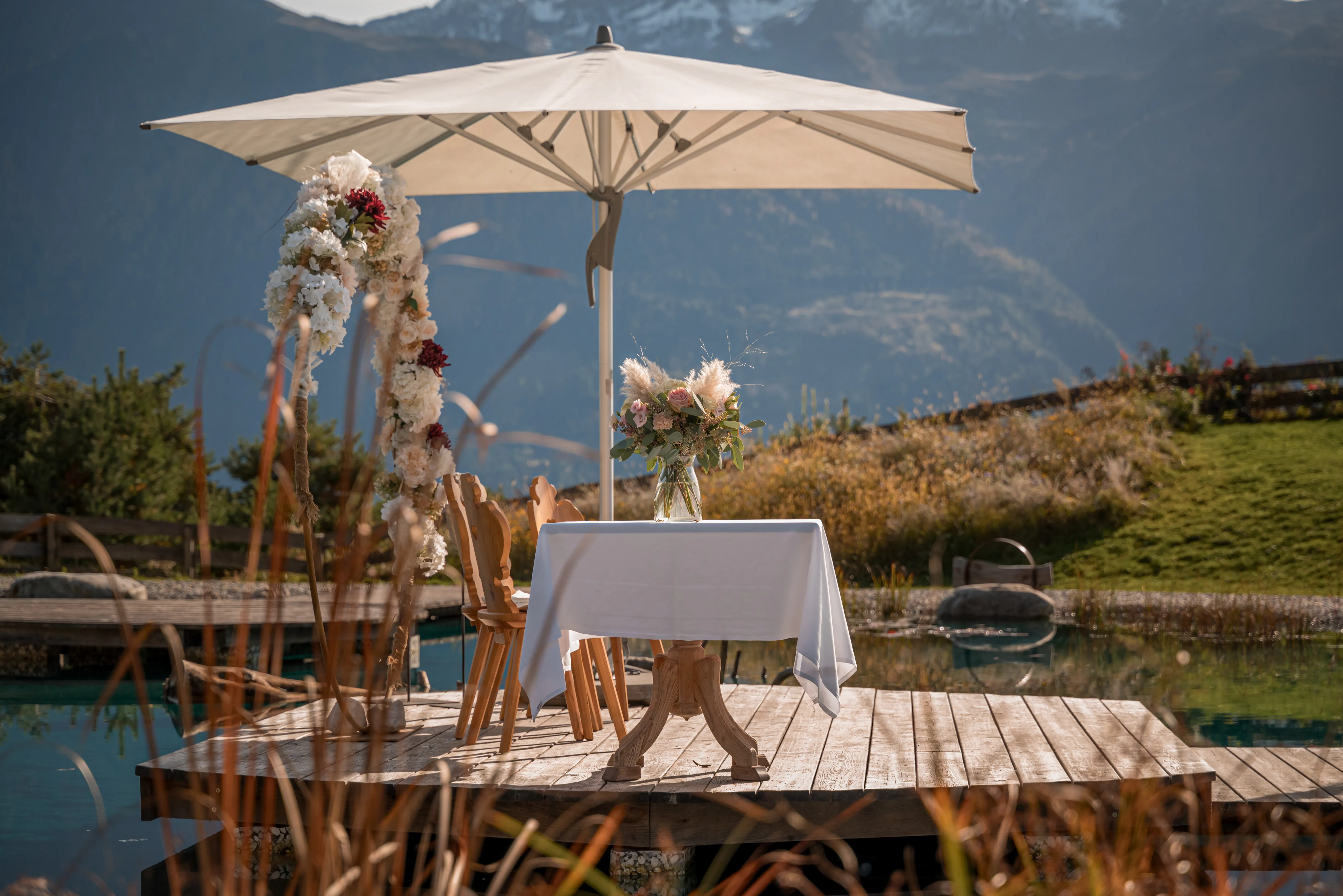 Romantisch gedeckter Tisch mit Blumenbogen auf dem Holzsteg am Naturteich der Stöttlalm